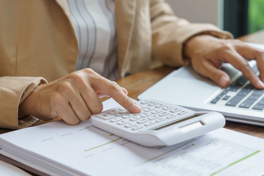 A person writing notes and using a laptop while reviewing financial documents, symbolising planning and budgeting for building a first home.