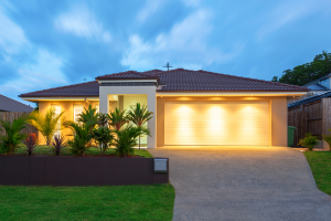 Modern single-storey suburban home at dusk with illuminated garage and landscaped front yard.