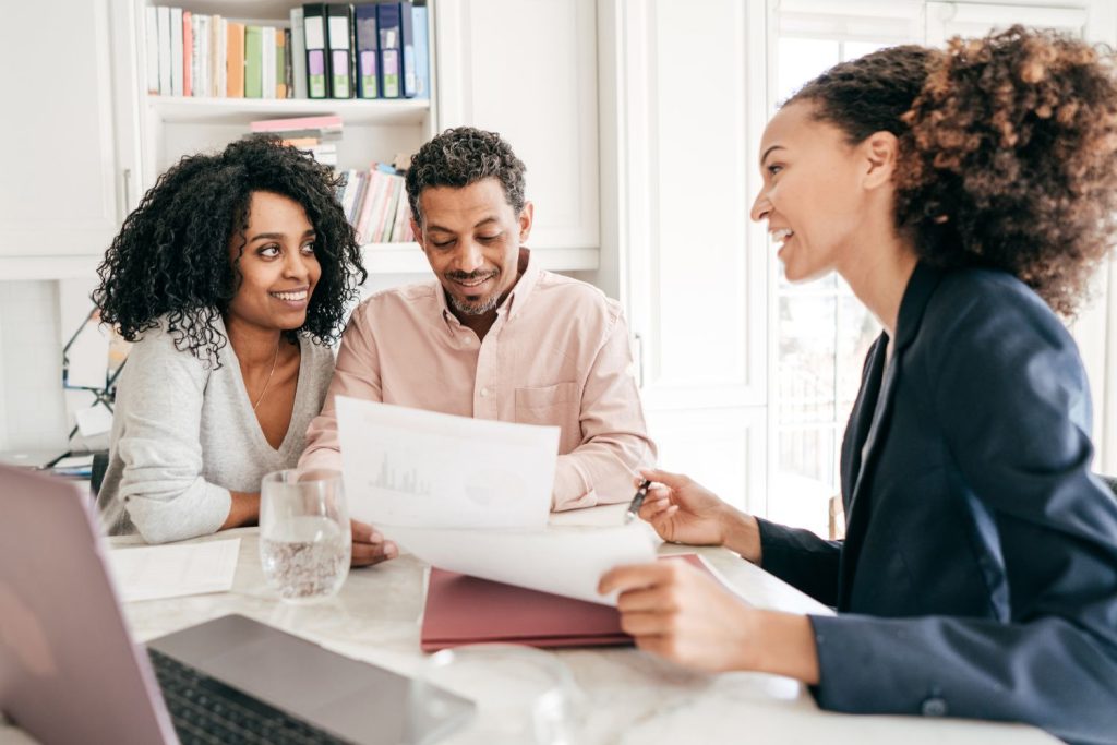 Two women and a man sitting together in a bright office, reviewing home loan documents and smiling during a discussion with a mortgage broker.