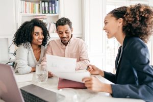 Two women and a man sitting together in a bright office, reviewing home loan documents and smiling during a discussion with a mortgage broker.